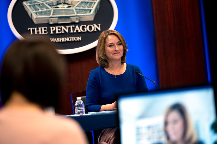 A woman participates in a virtual conversation. The sign behind her indicates that she is speaking from the Pentagon.