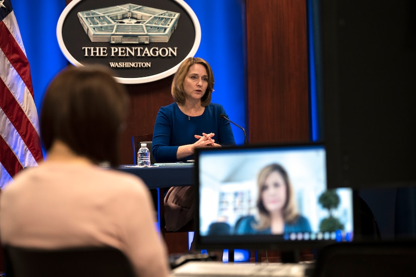 A woman participates in a virtual conversation. The sign behind her indicates that she is speaking from the Pentagon.