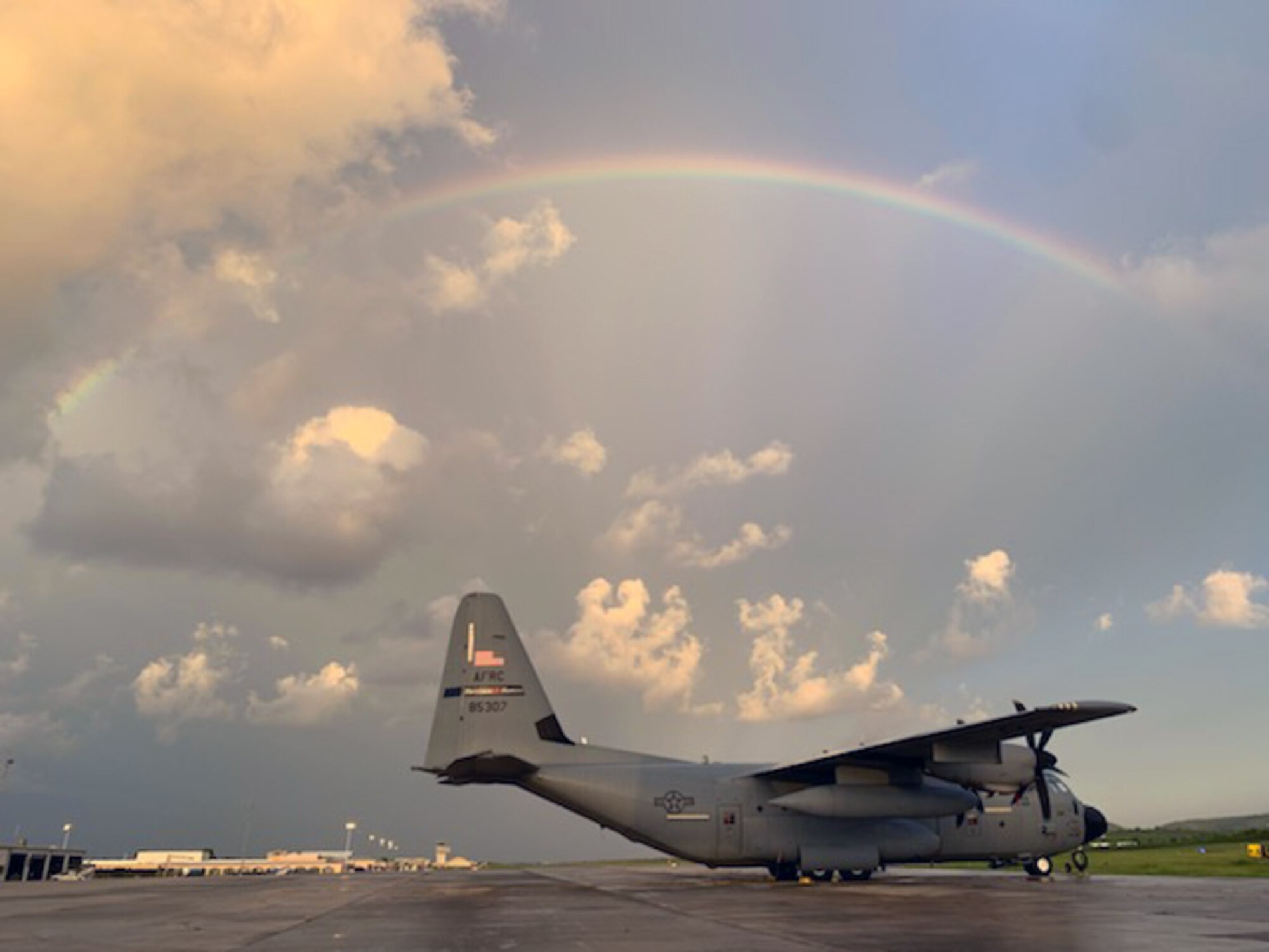 A WC-130J aircraft sits under a rainbow during at dusk.