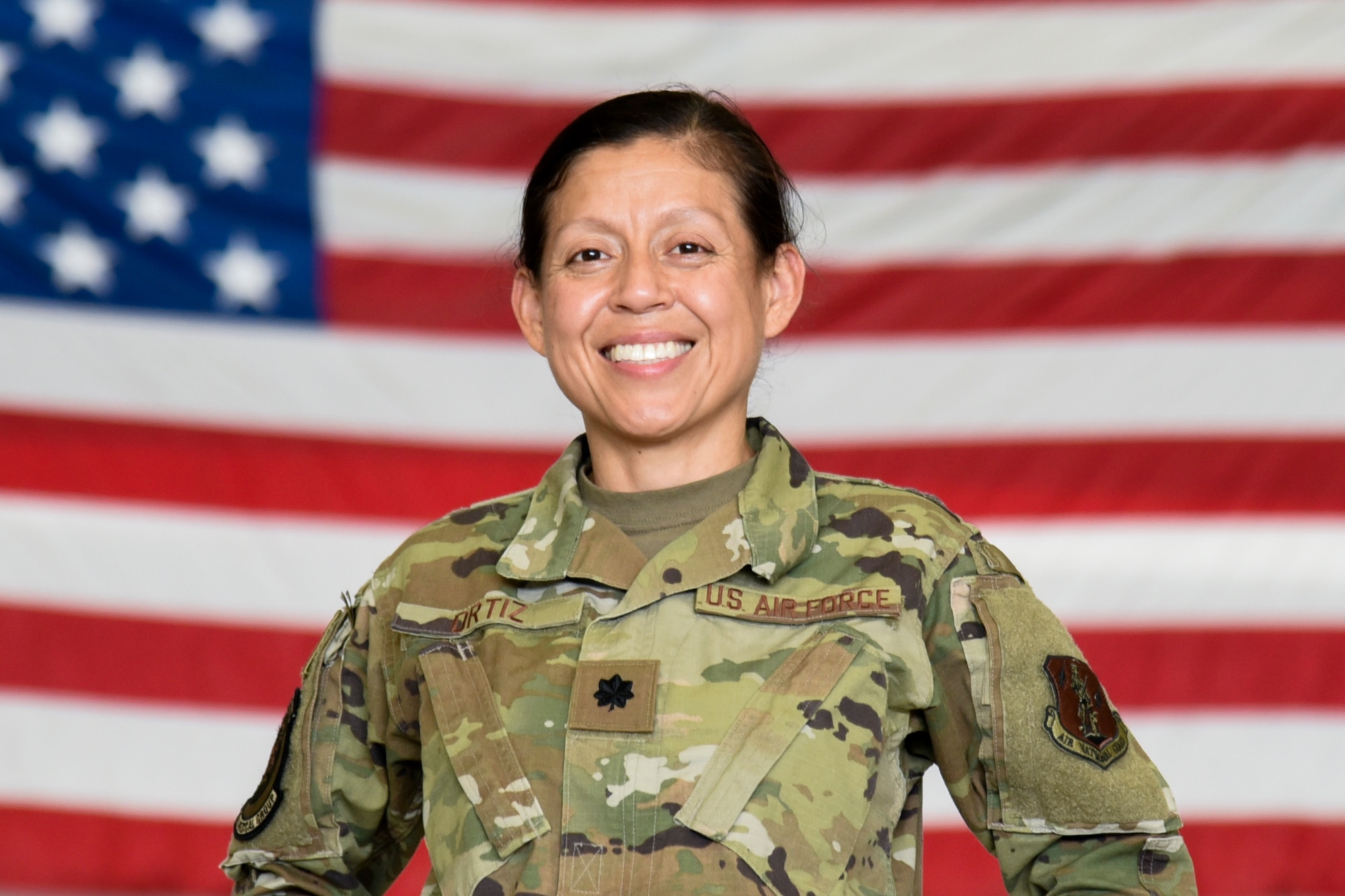 Lieutenant Colonel Daisy Ortiz poses in front of an American Flag in the security forces hangar on Joint Base McGuire-Dix-Lakehurst, October 2, 2021.