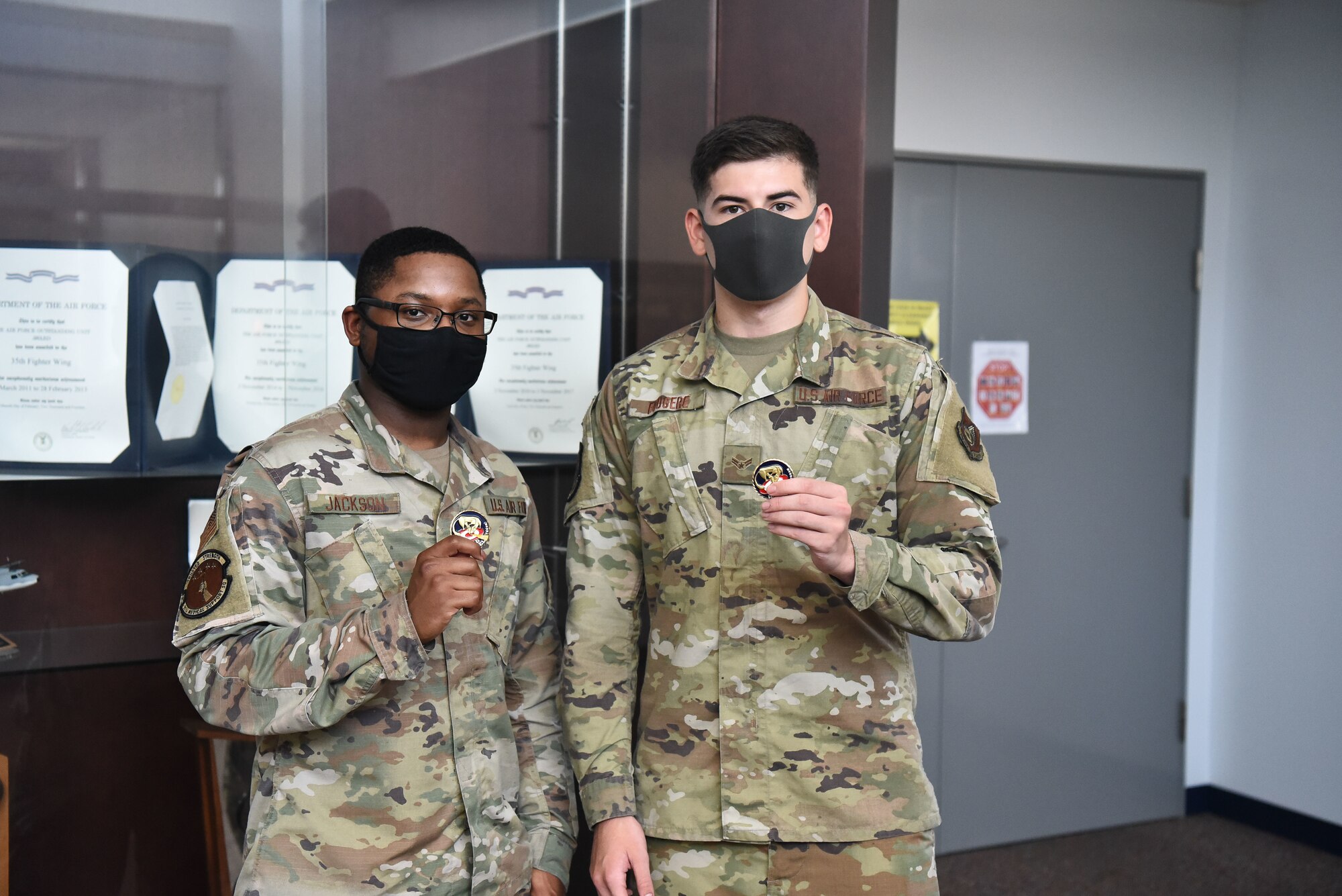 Two military members stand side by side displaying the coins they were awarded by the base commander
