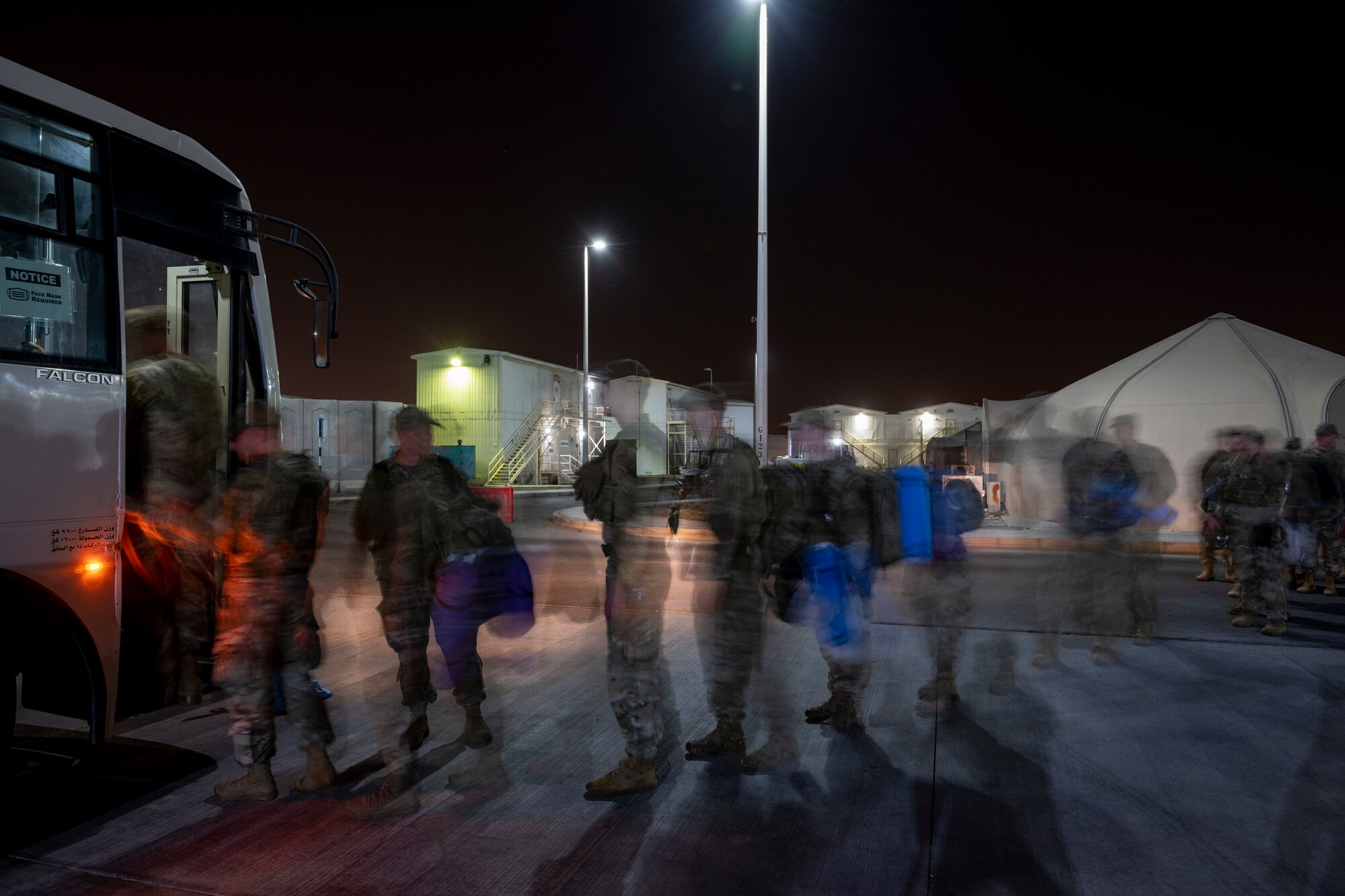 line of Airmen boarding a bus at night