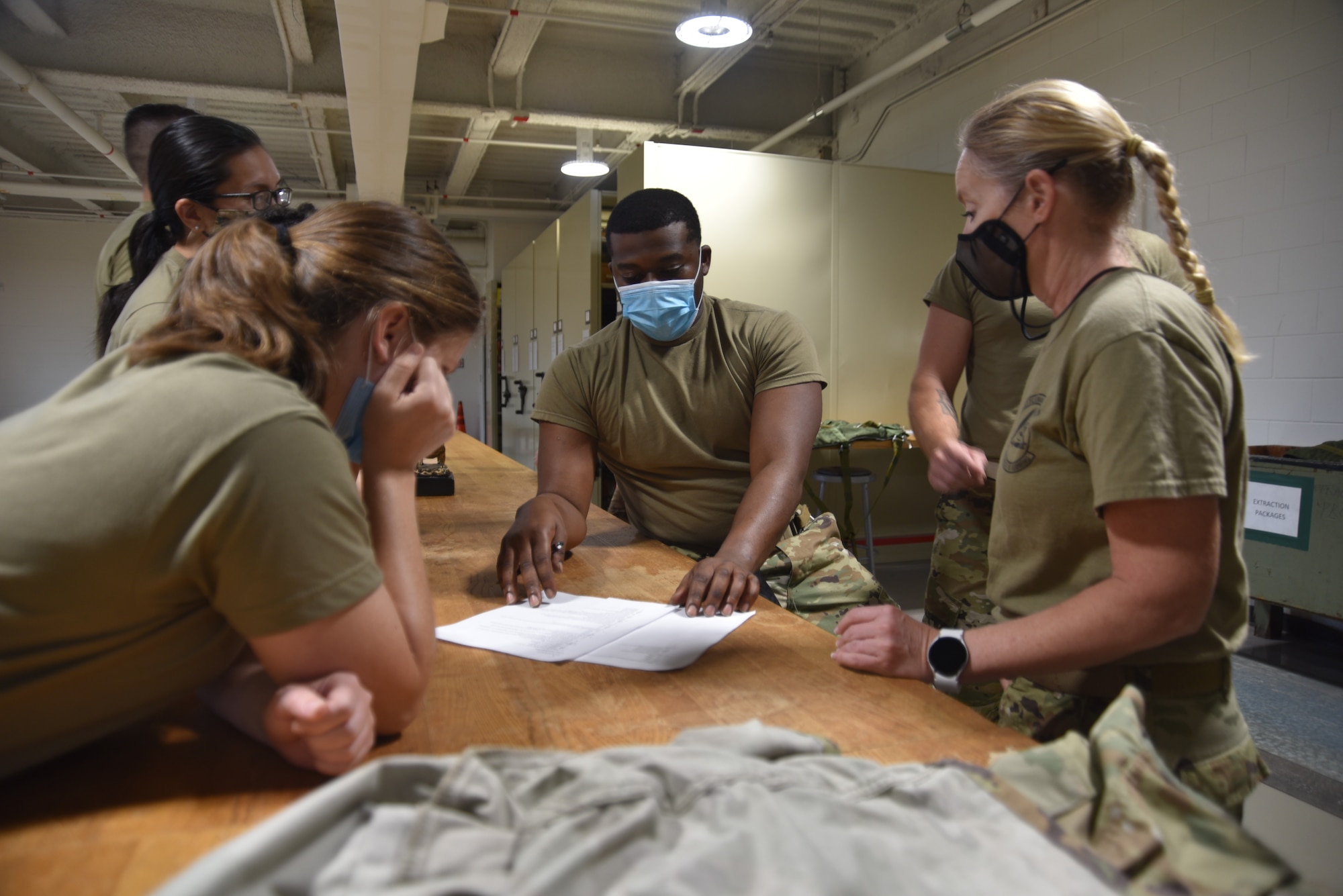 Six Airmen at a table look over a piece of paper.