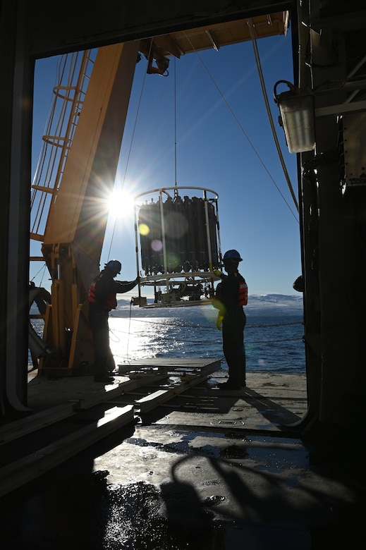 Two Coast Guardsmen hold a large device above the ocean.