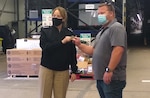 A woman poses with a man while both holding a coin in a warehouse.