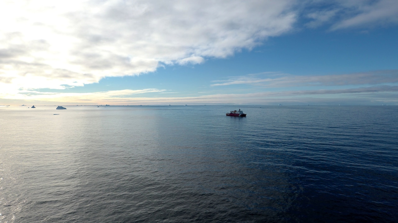 A wide view of a Coast Guard cutter navigating across a large expanse of water.