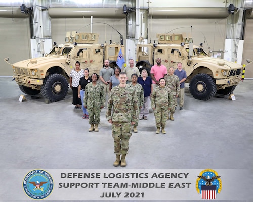 Men and women from DST-ME pose in front of military vehicles.