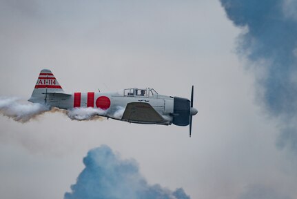 A vintage military aircraft flies to the right with clouds in the background