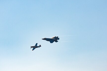 Two military aircraft, one vintage and one modern fly to the right