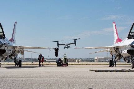 Military helicopter plane hovers the airfield in the background of two fighter jets.