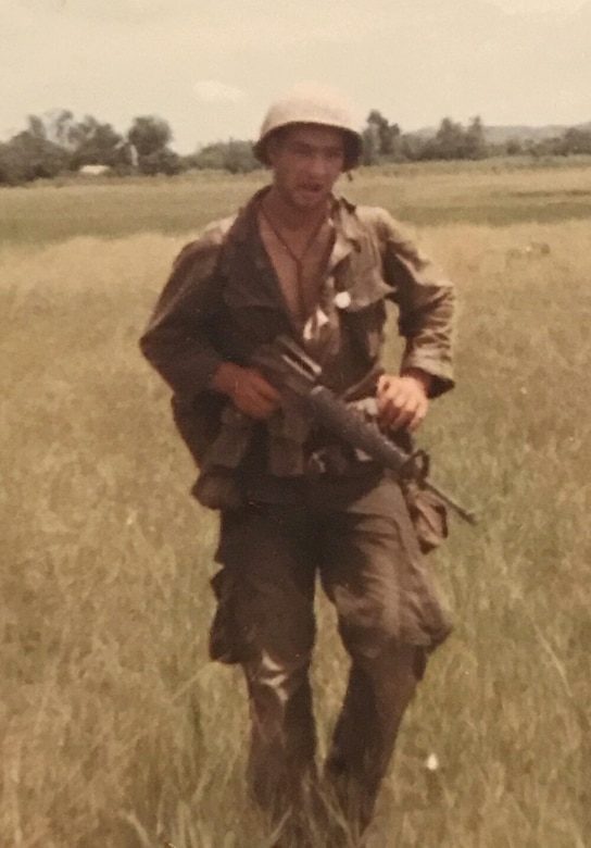 A Marine stands with a weapon in a field.