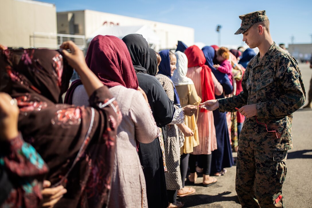 A Marine hands a ticket to a person standing in a line outside a building.