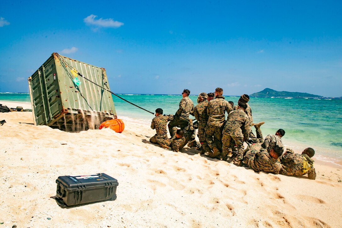 Marines pull a rope attached to a rig to lift it upright on a beach.