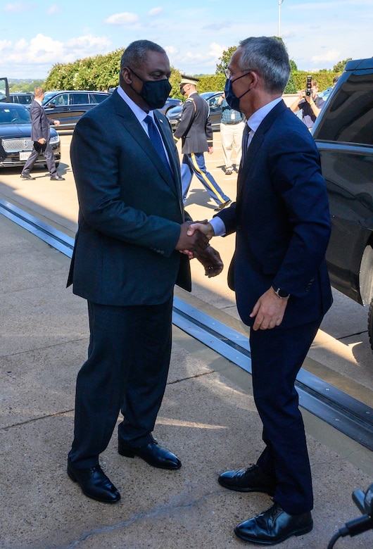 Two men shake hands outside a car.