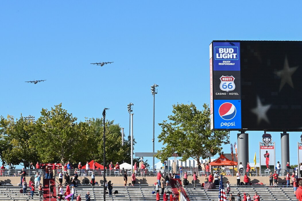 two large military aircraft flying over a college football stadium