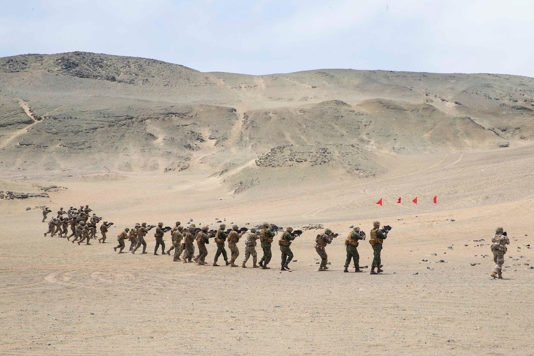 Troops move though desert terrain while holding weapons.