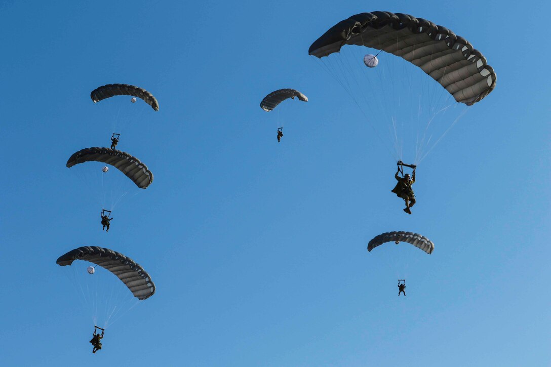 Soldiers descend in the air wearing parachutes.