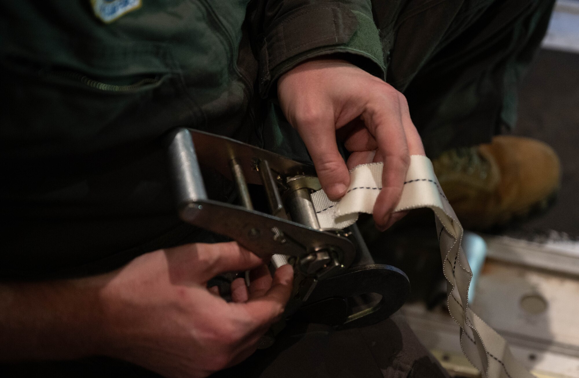 An Airman feeds a Type VII strap through a rachet.