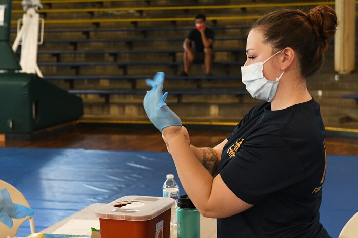 Hospital Corpsman Third Class Annemarie Dern from Navy Medicine Readiness and Training Command Pearl Harbor puts on gloves before administering a flu vaccine at Bloch Arena on October 4, 2021. Bloch Arena vaccination events will be held October 4-6, 12-13, and 25-27 from 7:30 am till 3:00 pm. Flu vaccines are mandatory for all active duty service members and the mass vaccination event at Bloch Arena will help facilitate larger commands.