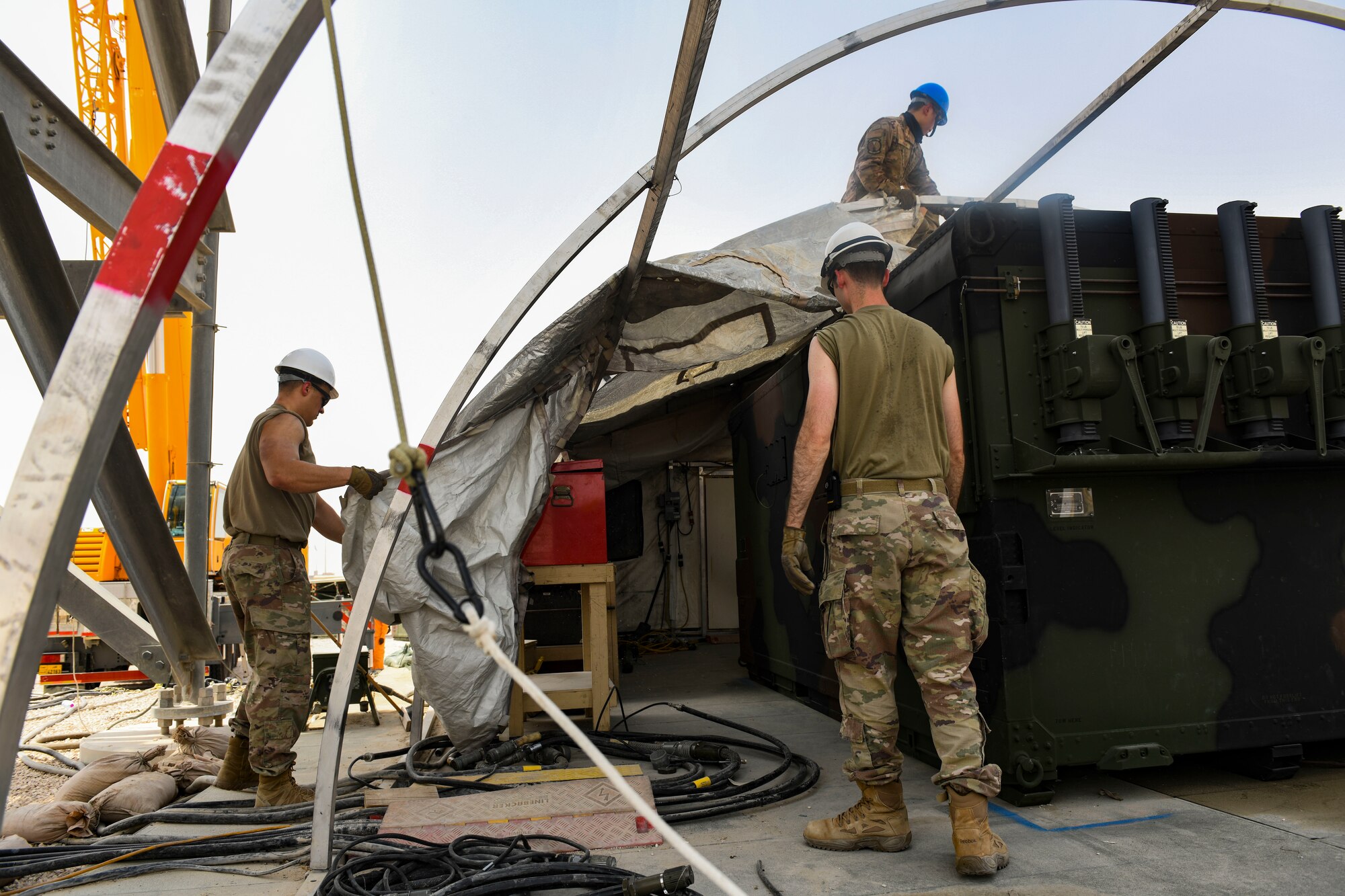 U.S. Air Force Senior Airman Anthony Niederschmidt, Airman 1st Class James Ballard, and Master Sgt. Jones Kwan, 727th Expeditionary Air Control Squadron, Detachment 3, radar technicians and superintendent, respectively, drag a protective covering into place over a shelter for a newly-replaced AN/TPS-75 radar system as part of regular maintenance July 27, 2021, at Al Udeid Air Base, Qatar. The radar provides a common surveillance and combat identification picture to support battle management command and control for the combined defense of the Arabian Peninsula. (U.S. Air Force by Staff Sgt. Alexandria Lee)
