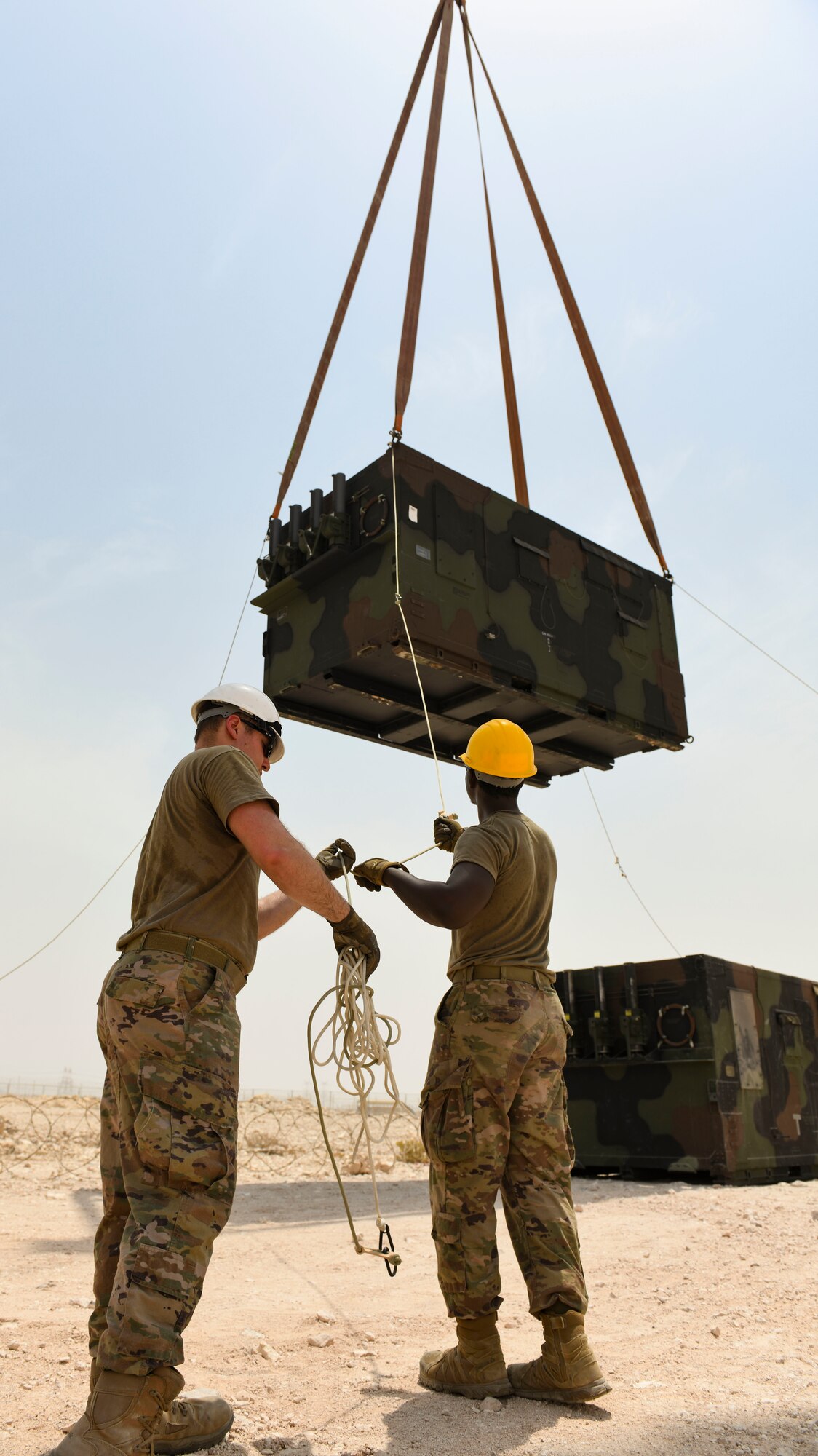 U.S. Air Force Airman 1st Class Alex Wolfe and Airman 1st Class Tahj Ballard, 727th Expeditionary Air Control Squadron, Detachment 3 radar technician and power production technician, respectively, pull tight a rope securing a new AN/TPS-75 radar system as it’s lowered into place July 27, 2021, at Al Udeid Air Base, Qatar. 727th EACS radar technicians perform several hours of maintenance and calibration daily to ensure the radar systems perform at optimal levels. (U.S. Air Force by Staff Sgt. Alexandria Lee)