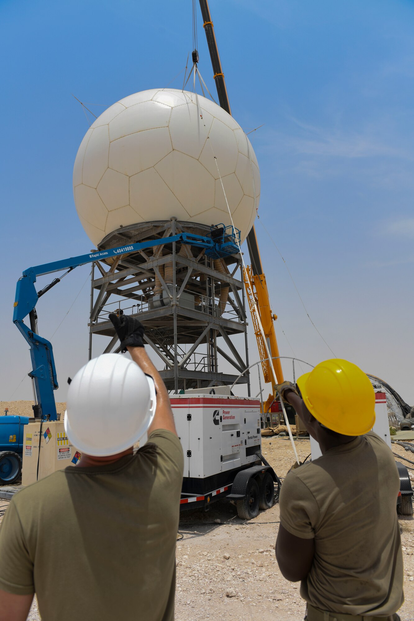 U.S. Air Force Airman 1st Class Alex Wolfe and Airman 1st Class Tahj Ballard, 727th Expeditionary Air Control Squadron, Detachment 3 radar technician and power production technician, respectively, help secure a radome as it’s lowered into place as part of regular maintenance July 27, 2021, at Al Udeid Air Base, Qatar. The 727th EACS radar technicians perform several hours of maintenance and calibration daily to ensure radar systems perform at optimal levels. (U.S. Air Force by Staff Sgt. Alexandria Lee)