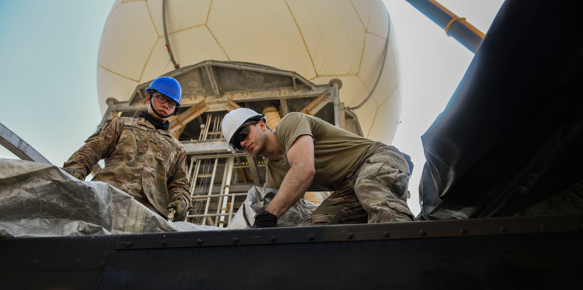 U.S. Air Force Master Sgt. Jones Kwan and Airman 1st Class Antonio De Simone, 727th Expeditionary Air Control Squadron, Detachment 3, superintendent and radar technician, respectively, drag a protective covering over a newly-replaced AN/TPS-75 radar system as part of regular maintenance July 27, 2021, at Al Udeid Air Base, Qatar. 727th EACS radar technicians perform several hours of maintenance and calibration daily to ensure radar systems perform at optimal levels. (U.S. Air Force by Staff Sgt. Alexandria Lee)