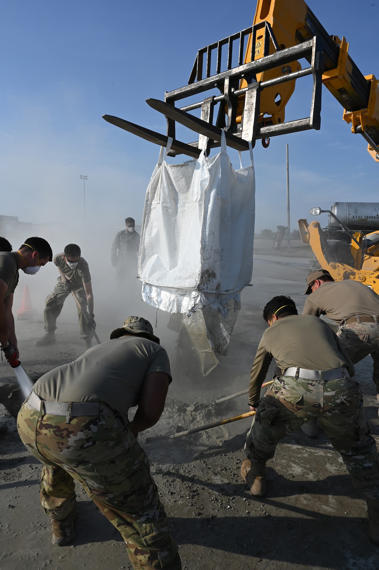 Five military members rake liquid concrete repair material as they smooth it into a square concrete hole in a concrete training runway at the North Dakota Air National Guard Regional Training Site, Fargo, N.D., Sept. 30, 2021.