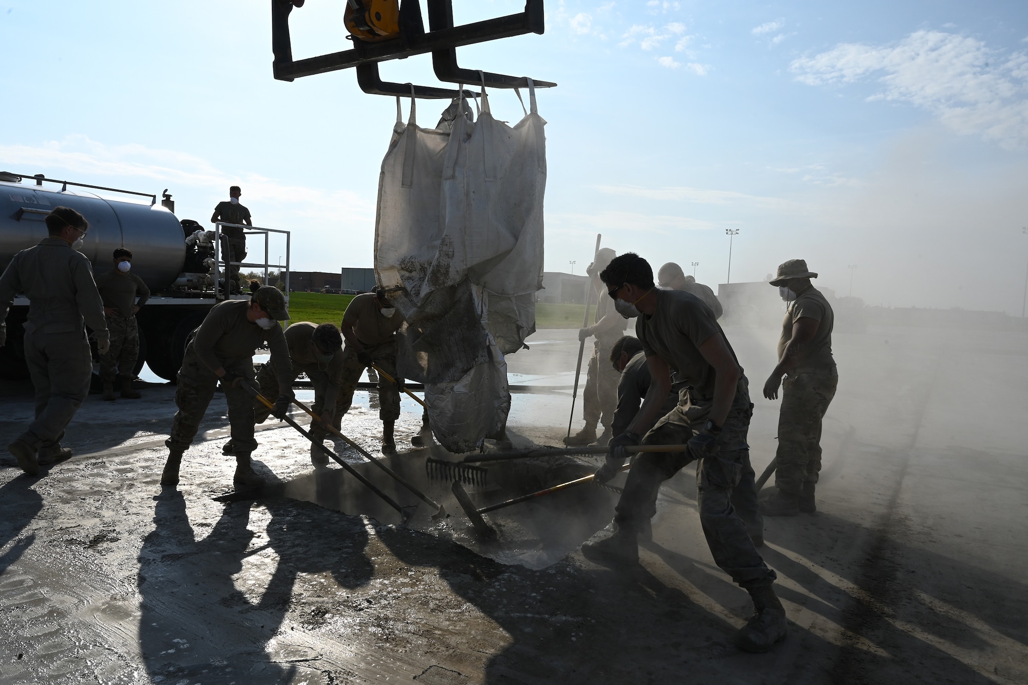 Eight military members rake liquid concrete material in a square hope on a concrete training runway at the North Dakota Air National Guard Base Regional Training Site, Fargo, N.D., Sept. 30, 2021.