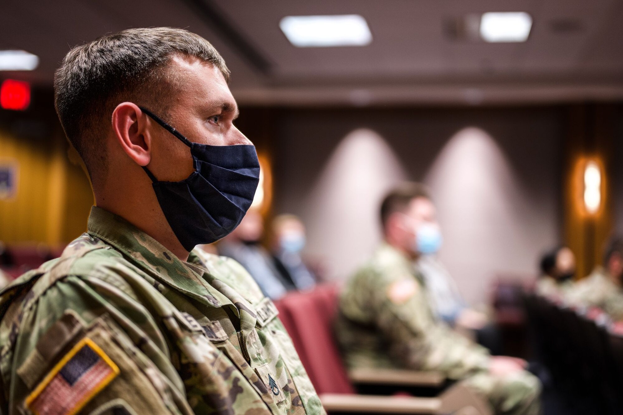A military member in a uniform sits in a conference room