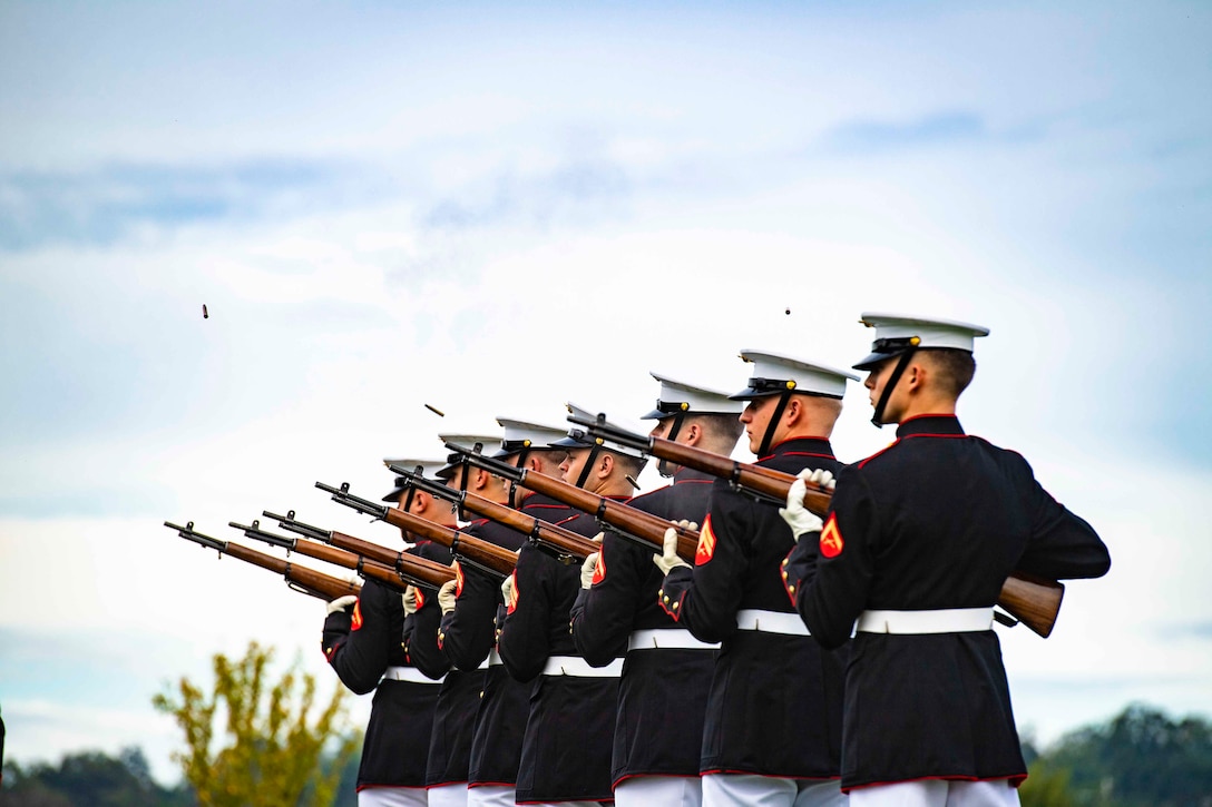 Marines stand in formation with their rifles pointed to the sky.