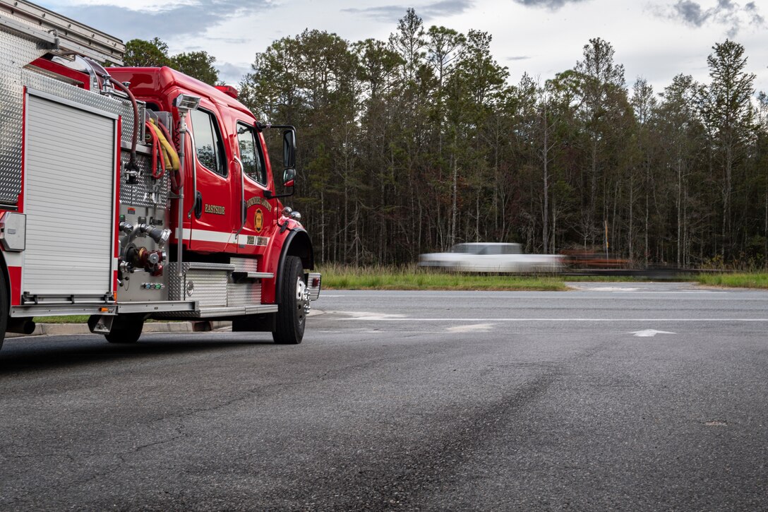 A fire truck sits in a driveway while a car drives past