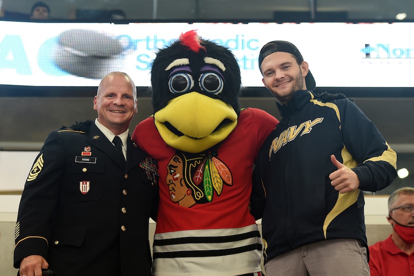 Sgt. Maj. Dennis Koski, left, operations sergeant major for the 85th U.S. Army Reserve Support Command, and U.S. Navy Veteran Lt. j.g. Ash Davis, meet Tommy Hawk, the Chicago Blackhawks’ mascot, after a military recognition during a Chicago Blackhawks NHL home game verses the St. Louis Blues, October 1, 2021.