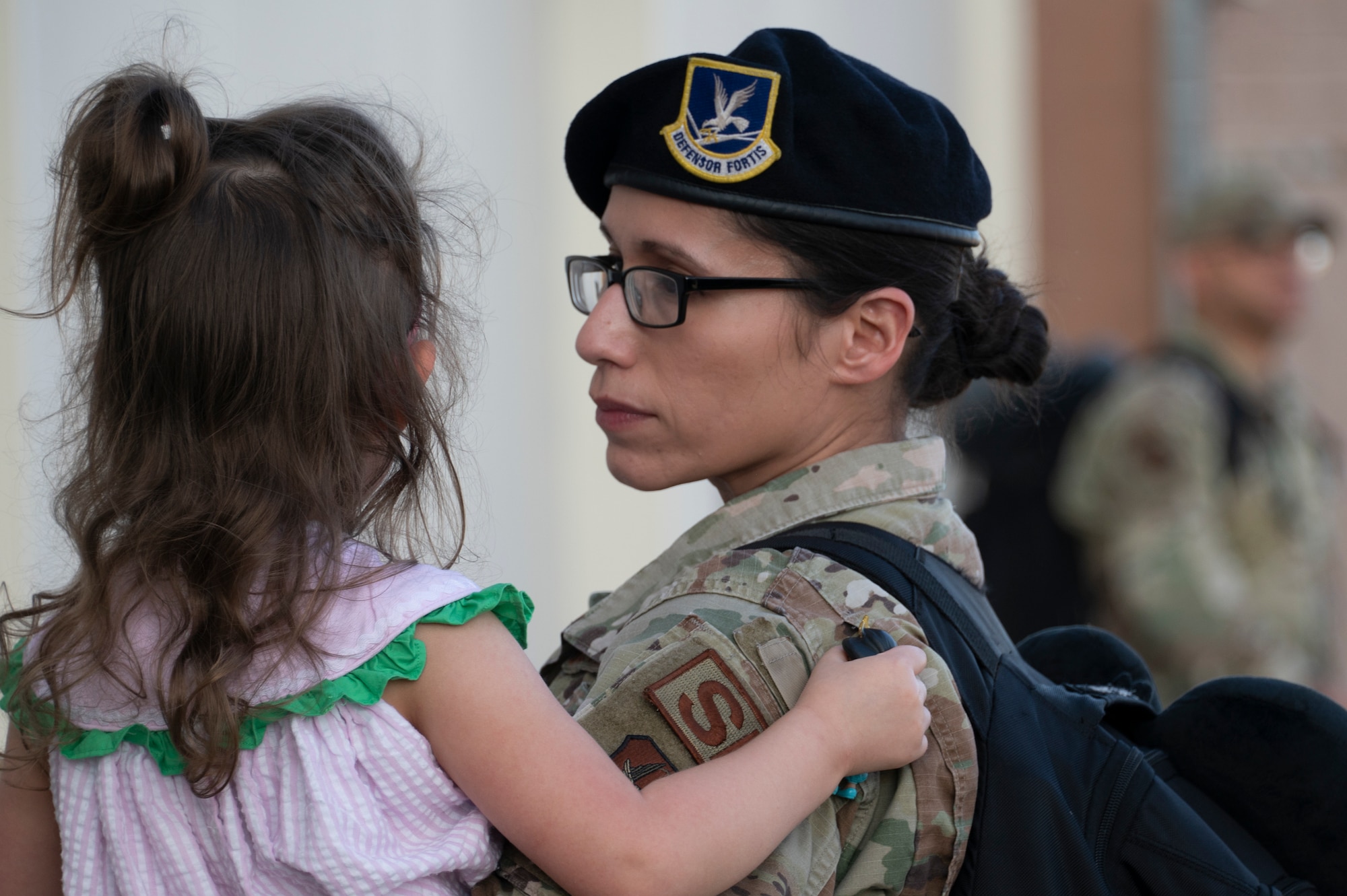 A mother in uniform holds her daughter.