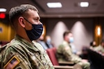 A military member in a uniform sits in a conference room