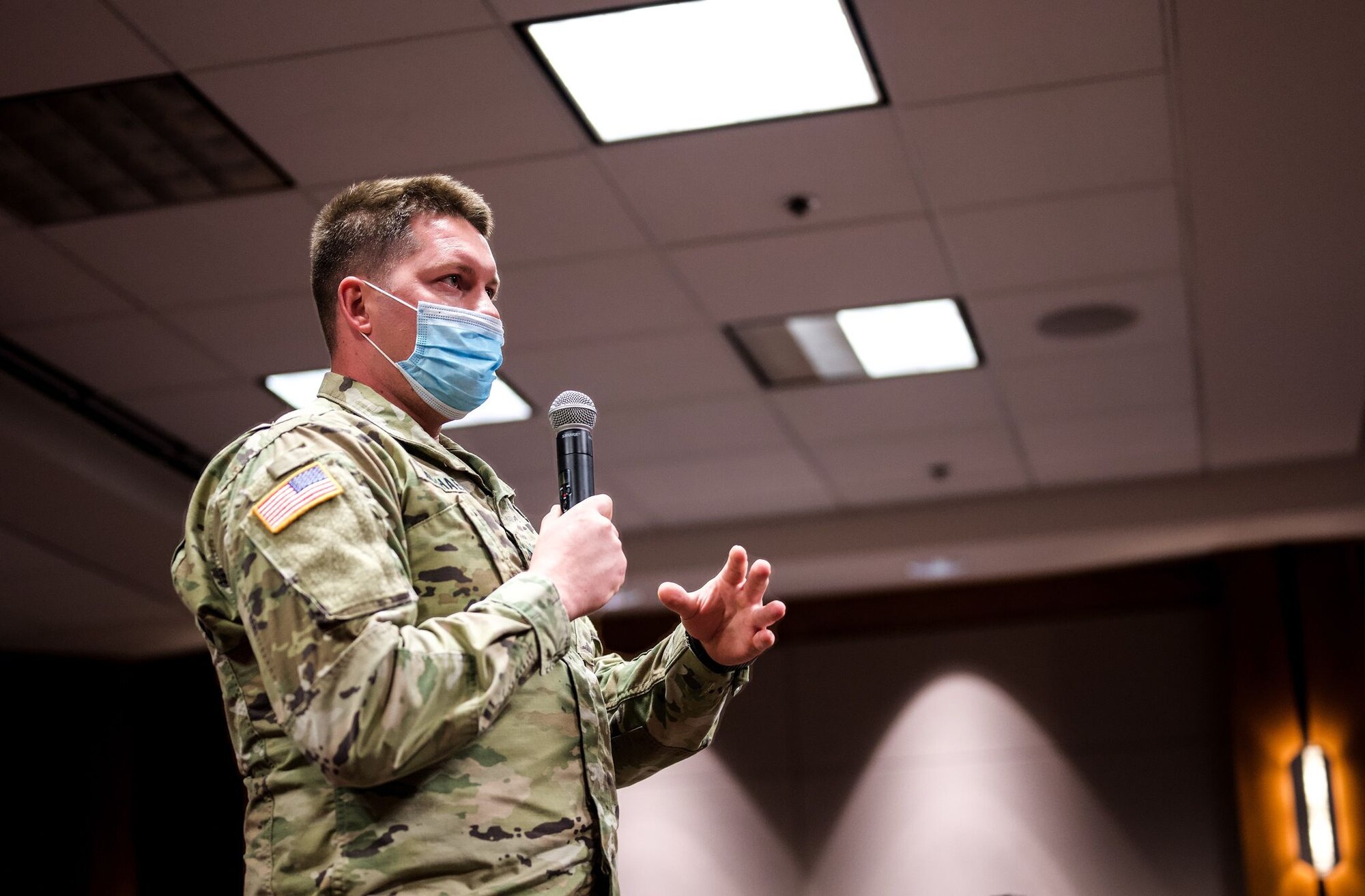 A uniformed service member addresses a crowd with a microphone in a conference room