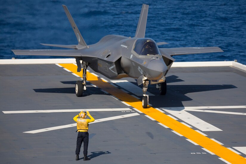 A sailor directs an F-35B Lightning II aircraft on the deck of a ship.