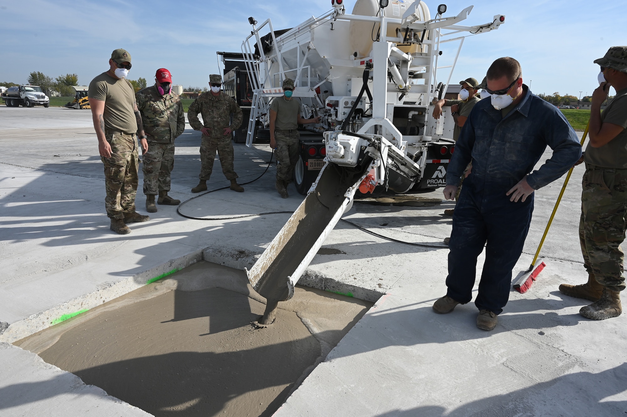 Three military members direct liquid concrete material into a square hole using a volumetric mixing machine to patch the hole in a concrete training runway at the North Dakota Air National Guard Regional Training Site, Fargo, N.D., Sept. 29, 2021.