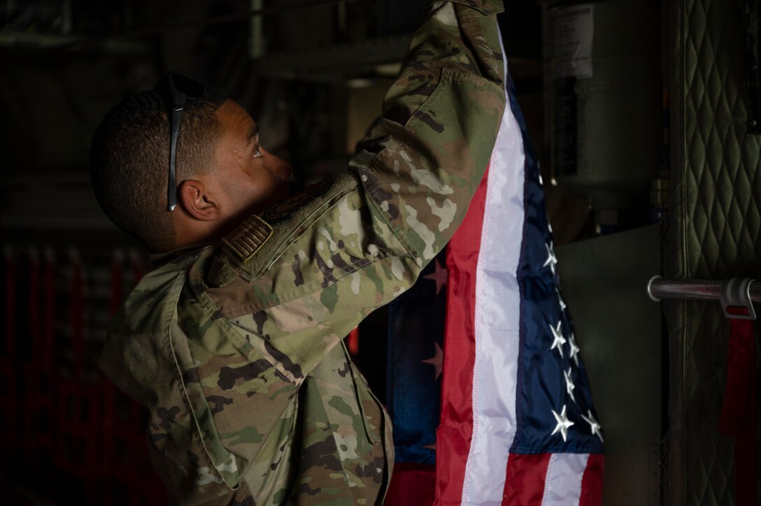 An Airman hangs the United States flag aboard a C-130H Hercules at Ali Al Salem Air Base, Kuwait, Sept. 16, 2021.