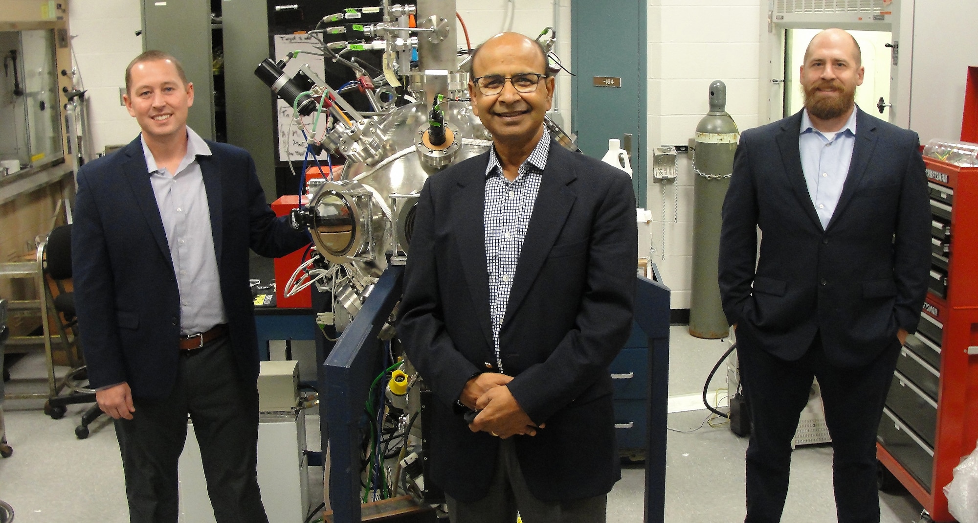 From left: Dr. Nick Glavin, Dr. Ajit Roy and Dr. Michael McConney stand with a nanomaterial deposition chamber at the Air Force Research Laboratory’s Materials and Manufacturing Directorate at Wright Patterson Air Force Base, Ohio, Sept. 24, 2021. The trio are increasing the availability of nano materials by building stronger ties with industry, government and academia in India. The Air Force Research Laboratory stood up a new Strategic Partnering Directorate, or AFRL/SP, to better achieve the Department of the Air Force’s mission and vision of collaborative science and technology partnerships. AFRL/SP will now manage international partnerships for the laboratory. (U.S. Air Force photo/Patrick Foose).