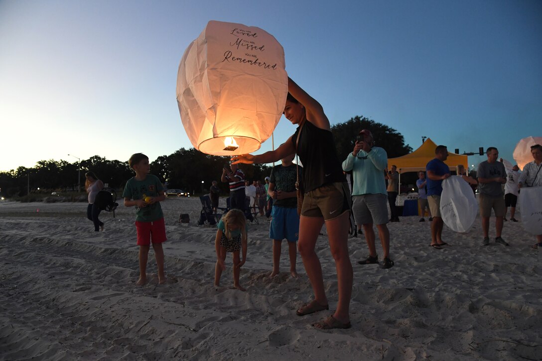 An airman prepares to release a lantern into the sky on the beach at dusk.