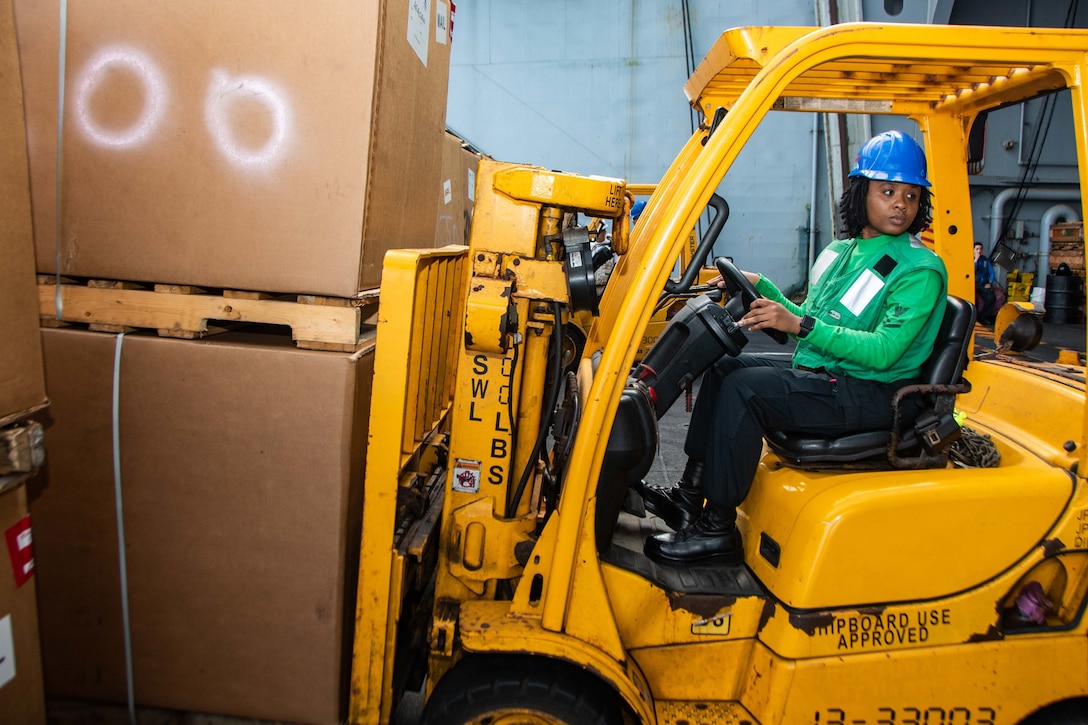 A sailor uses a forklift to move large boxes of mail.