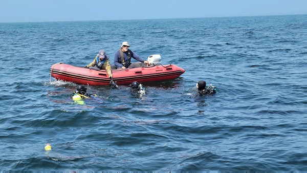 Blair Atcheson and Bill Graves lower tools to Navy divers over the shallow reef.