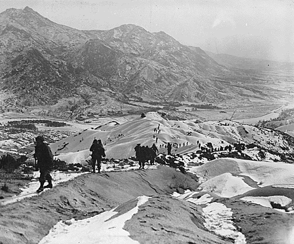 A line of soldiers walks along snow-covered crests. A large mountain is in the background.