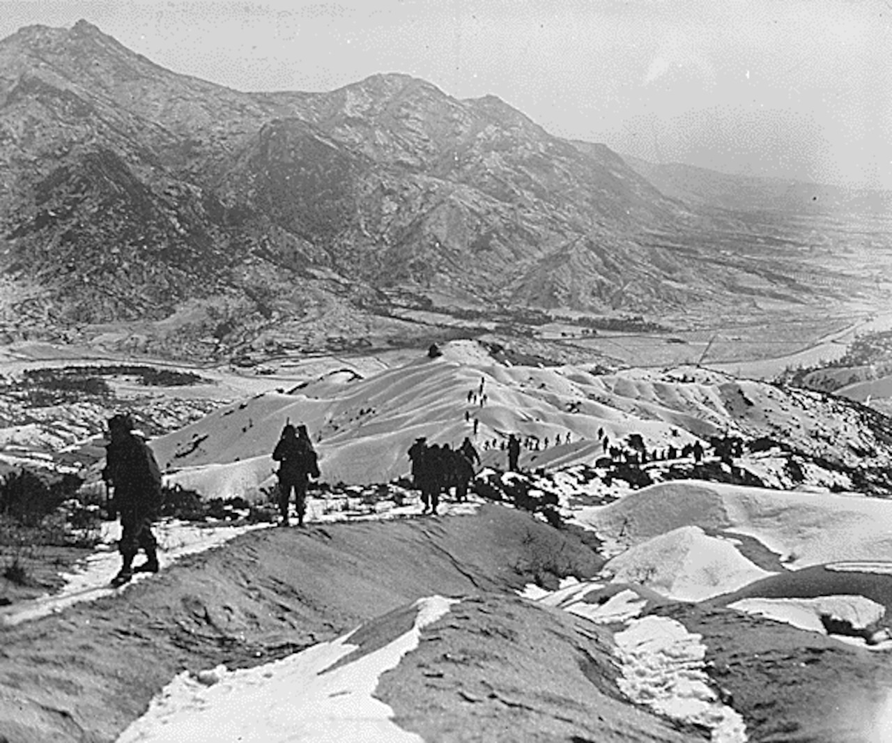 A line of soldiers walks along snow-covered crests. A large mountain is in the background.