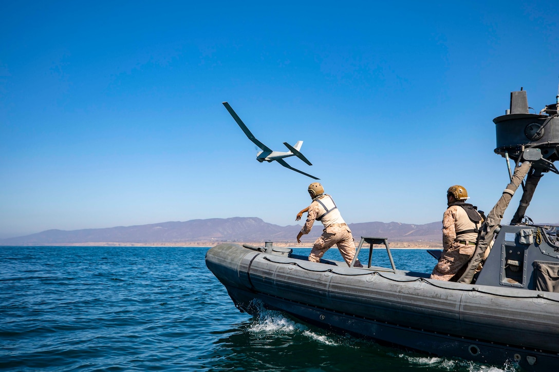 A Marine launches a small unmanned aircraft from an inflatable boat as others stand behind.