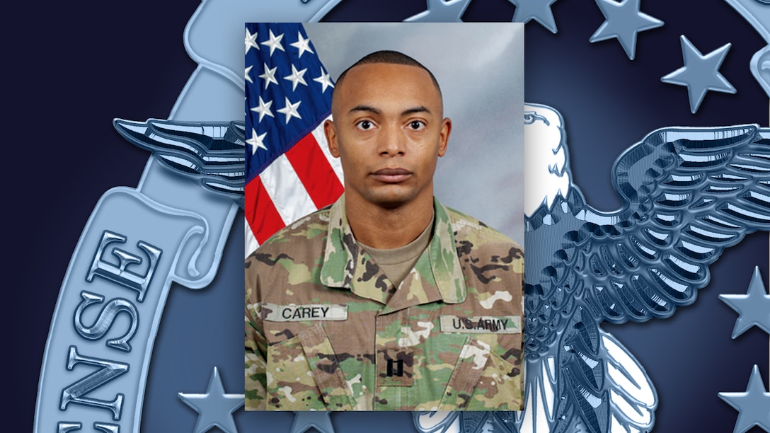 Head and shoulders picture of a black man in Army green camo uniform in front of the U.S. flag.