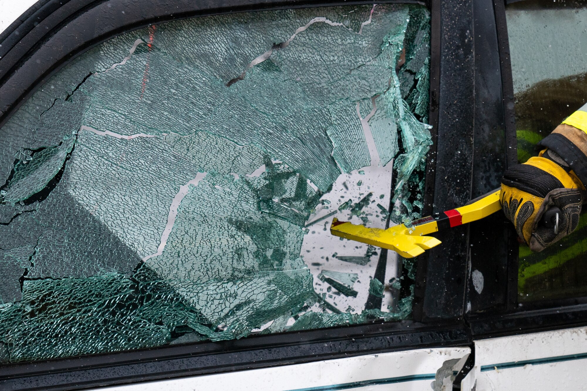 Nicholas Parks, a 673d Civil Engineer Squadron firefighter, uses a multitool to break the window of a damaged car for a vehicle-extrication demonstration during Fire Prevention Day.