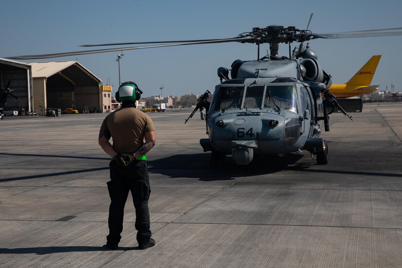 A soldier stands in front of a helicopter.