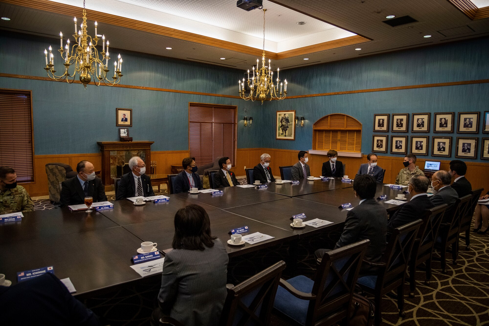Group of people in suits sit at a table with U.S. military members.